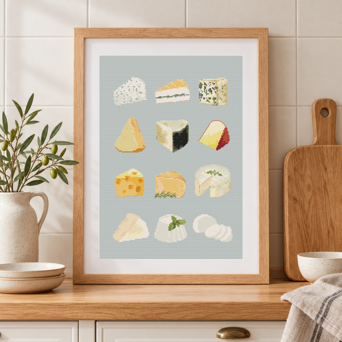 Framed cross stitch chart of various types of cheese on a light blue background